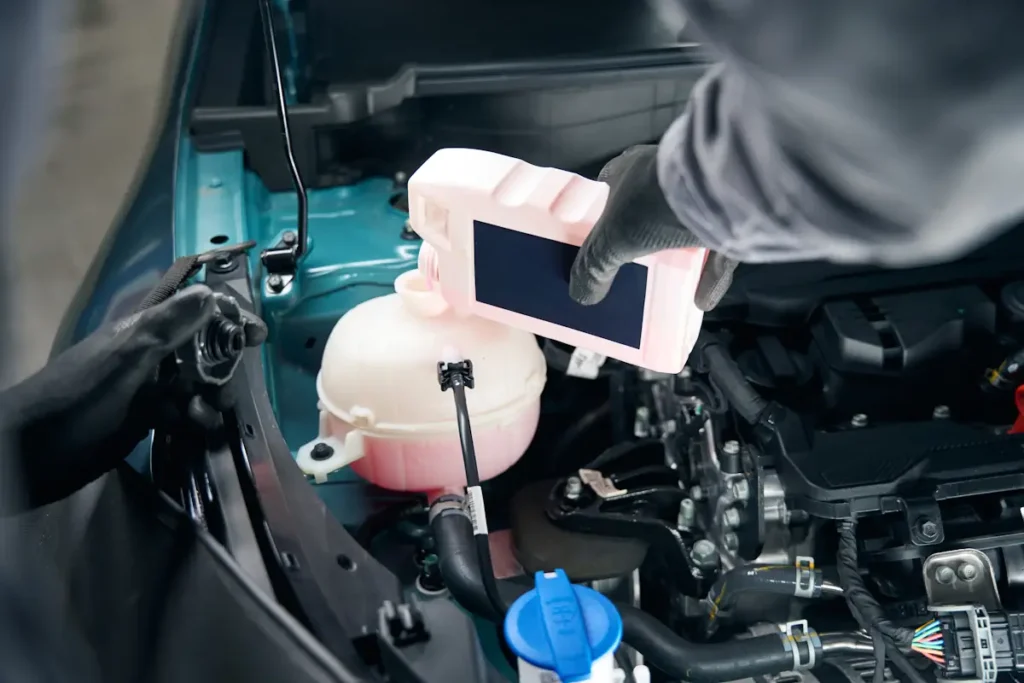 Une personne qui verse du liquide de refroidissement sous le capot d'une voiture