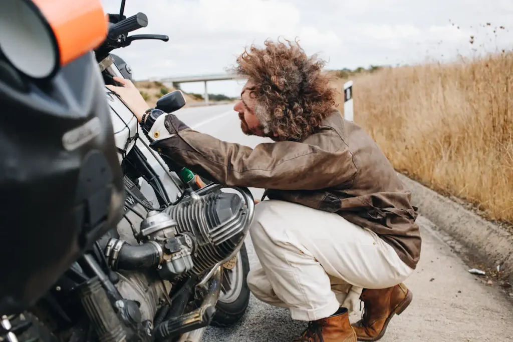 un homme qui regarde le moteur de sa moto garé sur le bas côté de la route