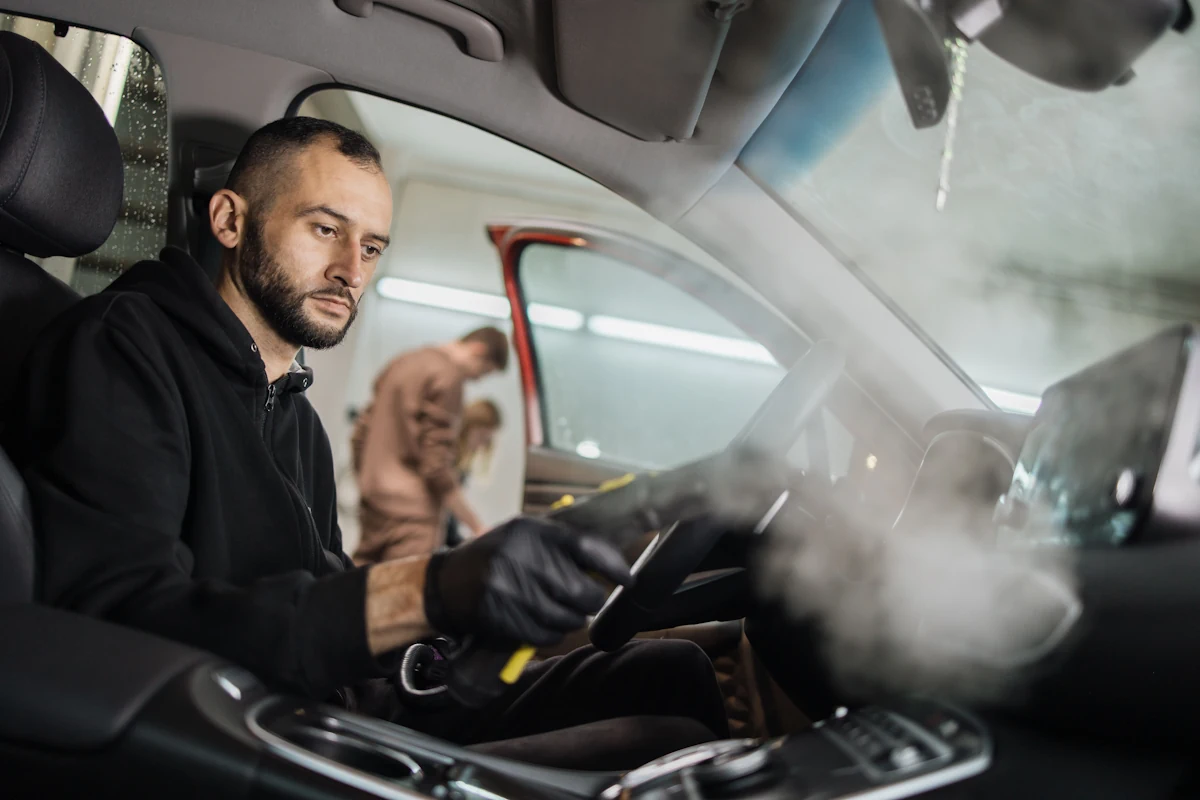 Un homme qui nettoie l'intérieur d'une voiture avec un appareil à vapeut